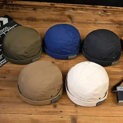 Five canvas docker caps in olive, navy, black, tan and cream on a wooden table